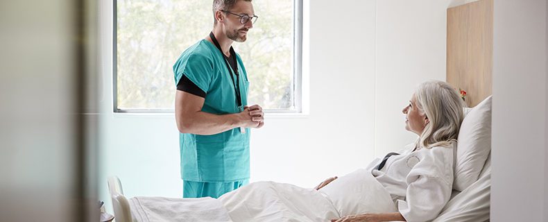 Male doctor speaking to female patient laying in hospital bed.