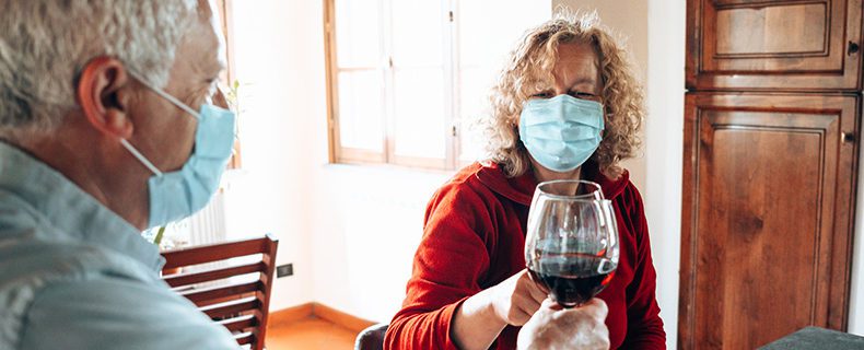 Two individuals in masks drinking wine.